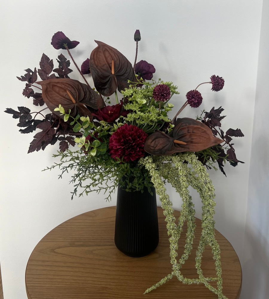 Standard fall arrangement: chocolate anthuriums, burgundy dahlias and green hydrangea with trailing amaranthus in a black vase